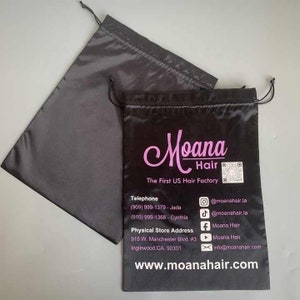 May include: Black satin drawstring bag with the text "Moana Hair The First US Hair Factory" printed in pink. The bag also includes contact information, including a phone number, email address, and social media handles.