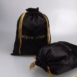 May include: Two black satin drawstring bags with gold ribbon ties. The larger bag has the text "elpre olen" printed in gold on the front.