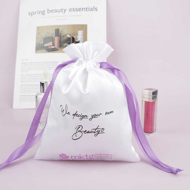 May include: White satin drawstring bag with a purple ribbon. The bag has the text "We design your own Beauty" printed on it in black with a small heart symbol. The bag also has the text "mktg industry" printed on it in pink.