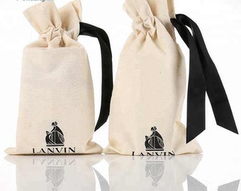 Op de afbeelding: Twee witte katoenen trekzakken met zwarte lintjes. Beide zakken hebben een zwart-wit logo met de tekst "LANVIN" en een gestileerd beeld van een vrouw.