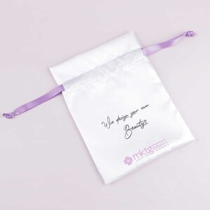 May include: White satin drawstring bag with a purple ribbon. The bag has the text "We design your own Beauty" and a logo that says "mktg industry creating in beauty".