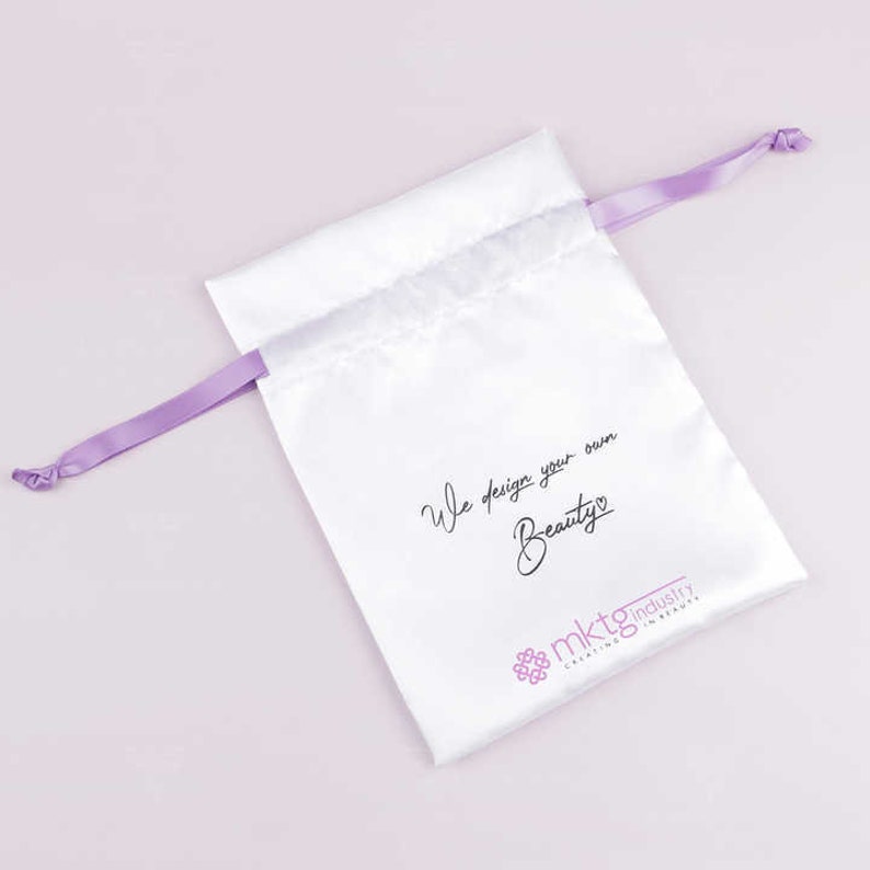 May include: White satin drawstring bag with a purple ribbon. The bag has the text "We design your own Beauty" and a logo that says "mktg industry creating in beauty".