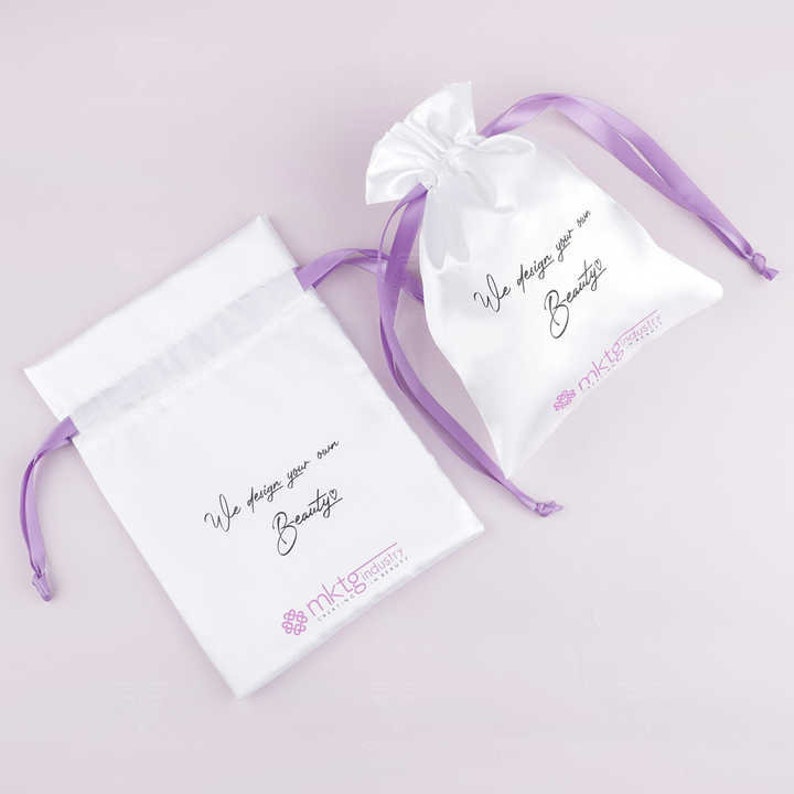 May include: Two white satin drawstring bags with purple ribbon ties. Both bags have the text "We design your own Beauty" and the logo "mktg industry" printed on them.