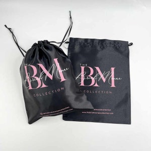 May include: Two black satin drawstring bags with the text "The Brush Monae Collection" and the logo "BM" in pink lettering.