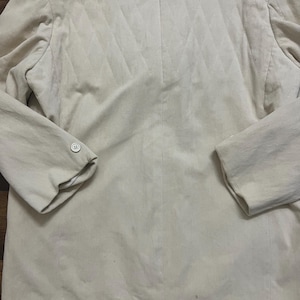 May include: A light beige corduroy blazer. The back panel features a quilted design. The blazer has long sleeves with buttoned cuffs and a notched lapel. The fabric has a vertical ribbed texture.