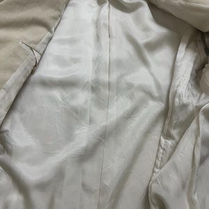 May include: Beige corduroy blazer with a white satin lining. The interior of the jacket is visible, showcasing the smooth, shiny texture of the lining. The blazer's exterior has a ribbed texture.