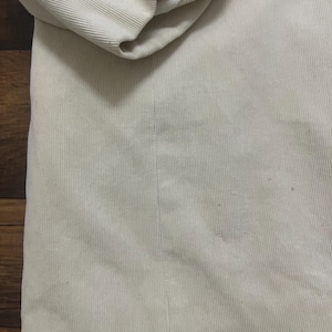 May include: A close-up view of a beige corduroy jacket. The jacket has a ribbed texture and a folded sleeve, showing a white lining. The fabric appears soft and has a slight sheen. The jacket is a neutral colour.