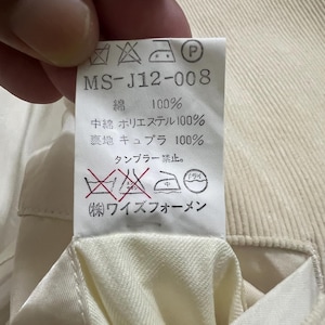 May include: A close-up of a cream-coloured fabric tag with Japanese text and care symbols. The tag reads "MS-J12-008" and lists fabric composition: 100% cotton, 100% polyester, and 100% cupro.