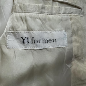 May include: Close-up of the interior of a light beige corduroy blazer. The lining is a lighter shade of beige. A white tag with the text "Y's for men" is sewn into the lining.