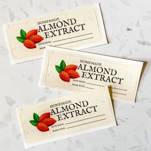 May include: Three blank labels with a cream background and brown text that reads "Homemade Almond Extract". Each label features a drawing of three almonds with green leaves.