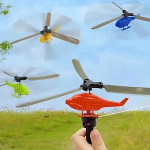Może przedstawiać: Kolekcja kolorowych helikopterów-zabawek w locie. Helikoptery są w różnych kolorach, w tym czerwonym, żółtym, zielonym i niebieskim. Śmigła się obracają, na tle błękitnego nieba i zielonej trawy.