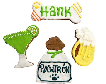 May include: A set of four dog treat cookies decorated with icing. The cookies are shaped like a bone, a margarita glass, a beer mug, and a bottle of tequila. The bone cookie is decorated with the name "Hank" and the tequila bottle cookie is decorated with the text "PAWTRÓN".