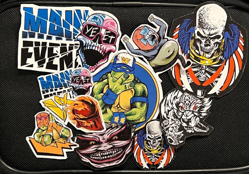 May include: A collection of colorful stickers featuring various characters and designs, including a skull with sunglasses, a Teenage Mutant Ninja Turtle, a skull with wings, and a monster with sharp teeth. The stickers are on a black background and have a variety of colors, including red, blue, green, yellow, and black.