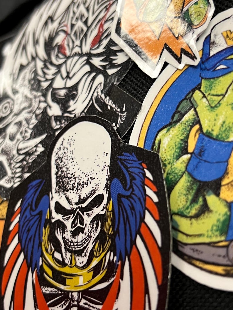 May include: A collection of colorful stickers featuring a skull with wings, a wolf, and a Teenage Mutant Ninja Turtle. The stickers are on a black background.