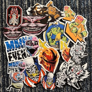 May include: A collection of colorful stickers featuring various characters and designs. Some of the stickers include a skull with sunglasses, a wrestler, a ninja turtle, and a wolf. The stickers are on a brown carpet.