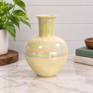 May include: A ceramic vase with a bulbous body and a flared rim, featuring a pale yellow base colour with a subtle iridescent, multi-coloured glaze overlay and a fine crackle texture throughout the entire surface of the vessel.