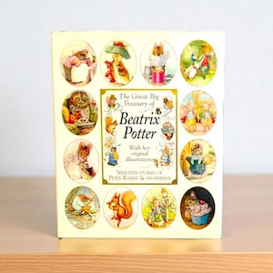 Peut inclure: Un livre à couverture rigide intitulé "The Great Big Treasury of Beatrix Potter" avec des illustrations de Pierre Lapin et ses amis. La couverture présente des illustrations ovales d'animaux en tenue colorée. Le livre est sur une surface claire.