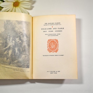 May include: An open book from "The Harvard Classics" series, titled "Folk-Lore and Fable." The book's pages are aged with text and illustrations. The cover features the text "ASOP GRIMM ANDERSEN" and a decorative emblem in orange.