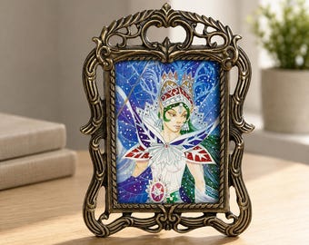 May include: A rectangular picture frame with an ornate, dark bronze-colored metal border featuring intricate scrollwork. Inside the frame is a colorful illustration of a figure with pointed ears, wearing a crown and a white collar against a blue background.