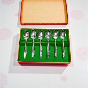 May include: A set of six silver spoons in a red and green box. The spoons are arranged neatly on a green felt-lined base. The box is open, revealing the spoons and a tan interior.