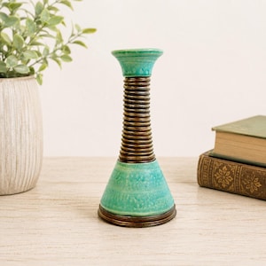 May include: A ceramic candlestick holder featuring a flared top and base in a bright turquoise glaze. The central column is composed of a series of stacked, dark brown, ribbed rings that create a textured, cylindrical appearance throughout the middle.