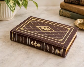 May include: A brown hardcover book titled The Harvard Classics Director's Edition with gold foil diamond grid patterns on the cover and spine. The spine features decorative gold filigree accents and text, with gold-edged pages visible on the side.
