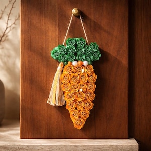 May include: A decorative carrot-shaped wall hanging made of orange and green paper roses. The carrot has a green top, orange body, and a tassel. It hangs from a gold hook on a wooden door.