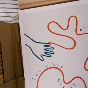 Pu&ograve; includere: Un'illustrazione disegnata a mano di una mano collegata a uno spago rosso che dice "invisible string" e continua a formare un cuore. Lo spago dice anche "all" e "string".