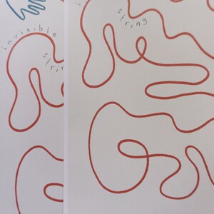 Pu&ograve; includere: Uno sfondo bianco con uno spago rosso disegnato in una linea continua che forma una serie di anelli e curve. Il testo "invisible string" &egrave; scritto in blu lungo lo spago.