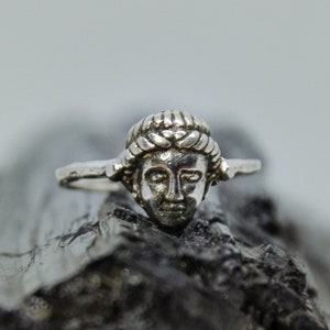 May include: A silver ring with a detailed sculpted face of a woman with a crown of leaves.