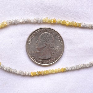 May include: A strand of rough, unpolished diamonds, some clear and some yellow, laid out on a white surface next to a US quarter for scale.