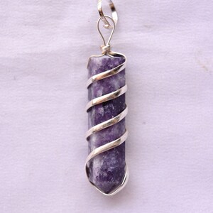 May include: A purple crystal pendant wrapped in silver wire. The crystal is a long, thin point with a silver bail at the top.
