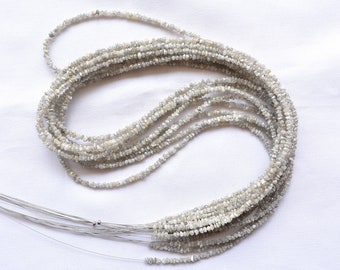 May include: A strand of rough, white diamond beads. The beads are small and irregular in shape, and they are strung on a thin wire. The beads are arranged in a loose, flowing pattern.