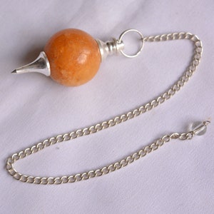 Könnte beinhalten: Ein silbernes Kettenpendel mit einem runden, orangebraunen Stein daran. Die Kette hat eine kleine, klare Kristallperle am Ende.