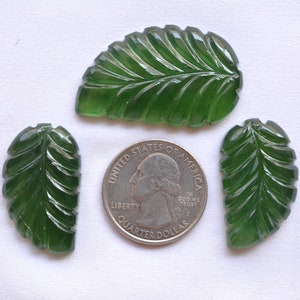 Puede incluir: Tres colgantes de piedra preciosa de forma de hoja tallados en verde, cada uno con un patrón de vetas detallado, junto a una moneda de veinticinco centavos de dólar estadounidense para comparar el tamaño.