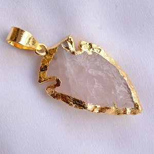 May include: A pink rose quartz arrowhead pendant with a gold-plated edge. The pendant is attached to a gold-plated bail.