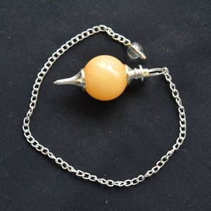 Könnte beinhalten: Eine silberne Kette mit einem hellorangenen Kristallkugel-Pendel. Das Pendel hat eine silberne Spitze unten und einen silbernen Ring oben.