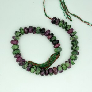 May include: A strand of green and purple gemstone beads with a green and red tassel. The beads are faceted and have a speckled appearance.
