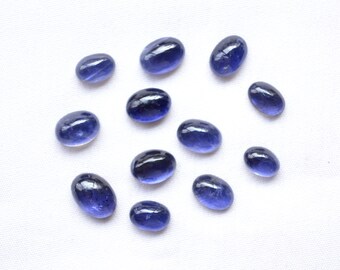 May include: A collection of twelve oval-shaped, blue gemstones. The gemstones are arranged in a circle on a white surface.