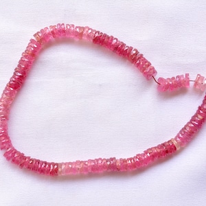May include: A strand of pink gemstone beads, likely tourmaline, with a faceted, slightly irregular shape. The beads are strung on a wire and are ready for jewelry making.
