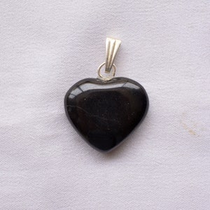 May include: A black heart-shaped pendant with a silver bail. The pendant is made of polished stone and has a smooth, glossy finish.