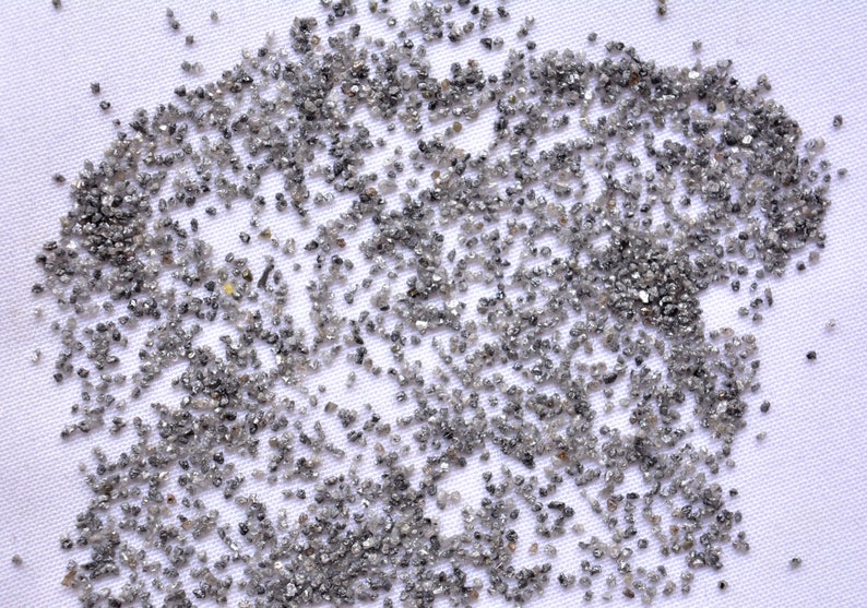 Pode incluir: Um close-up de uma superf&iacute;cie branca coberta de pequenos diamantes cinzentos. Os diamantes est&atilde;o espalhados aleatoriamente pela superf&iacute;cie, criando um efeito brilhante.