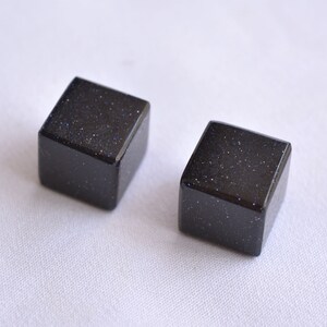 Puede incluir: Dos pequeñas piedras cuadradas de color azul oscuro, pulidas y con una textura brillante.