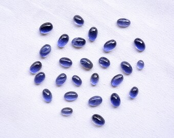 May include: A collection of oval-shaped, blue gemstones scattered on a white fabric background.