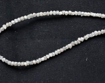 May include: A strand of white rough diamonds strung together on a thin wire. The diamonds are small and irregular in shape, and they have a slightly cloudy appearance.