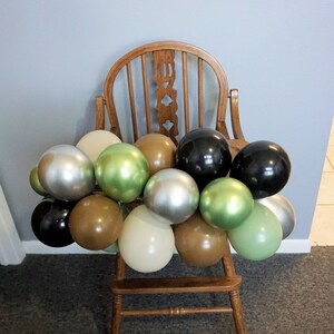 May include: A wooden high chair decorated with a garland of balloons in various colours, including silver, green, brown, and black.