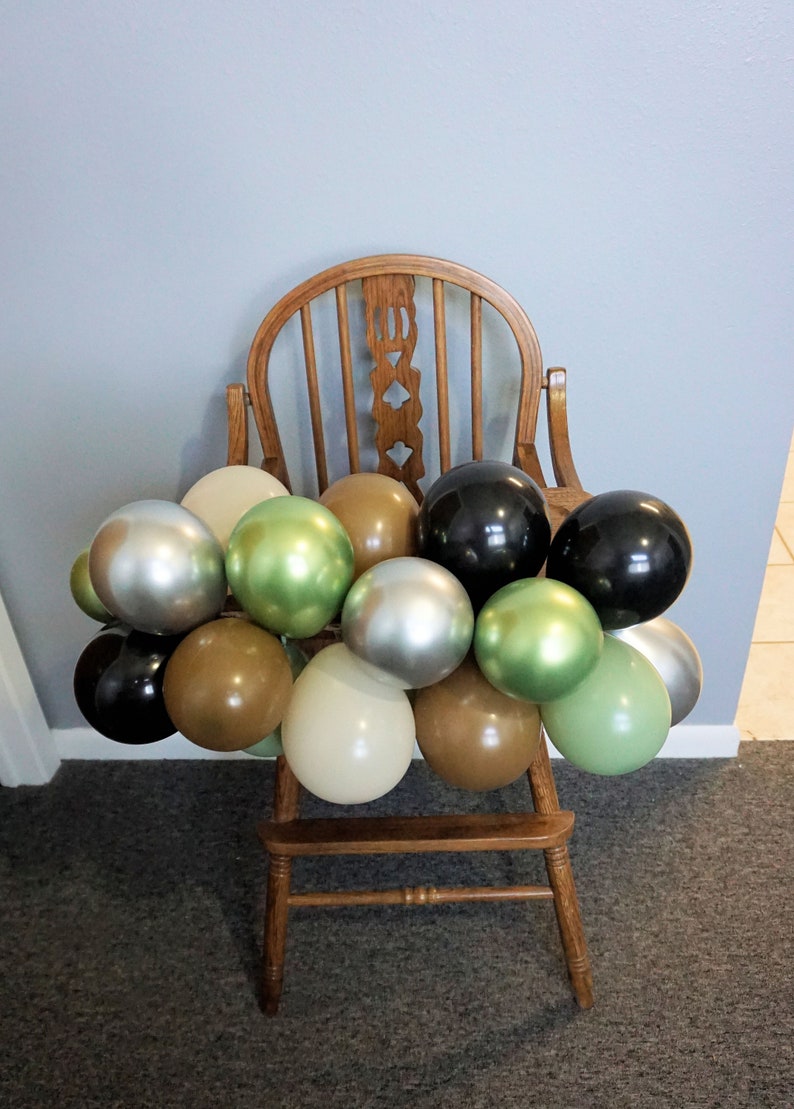 May include: A wooden high chair decorated with a garland of balloons in various colours, including silver, green, brown, and black.