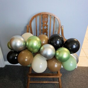 May include: A wooden high chair decorated with a garland of balloons in various colours, including black, silver, brown, green, and cream.