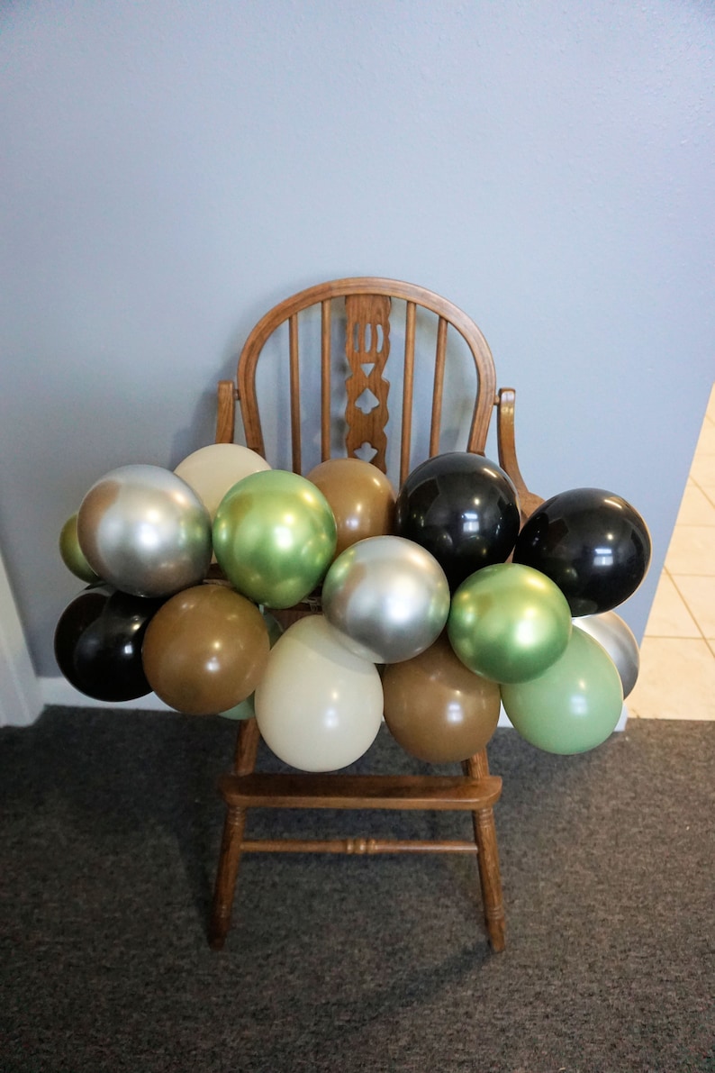 May include: A wooden high chair decorated with a garland of balloons in various colours, including black, silver, brown, green, and cream.
