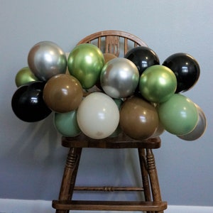 May include: A wooden chair decorated with a garland of balloons in various colours, including black, silver, green, brown, and cream.